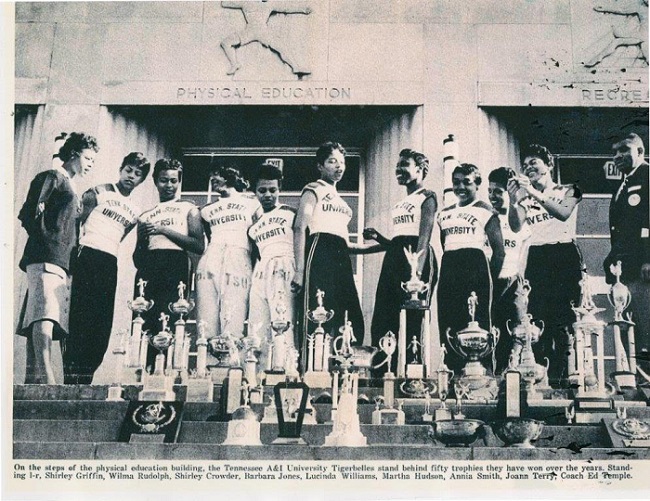 Tigerbelles women's track team standing behind fifty trophies they won over the years with their coach/Courtesy Aime Alley Card, author of The Tigerbelles, Olympic Legends from Tennessee State